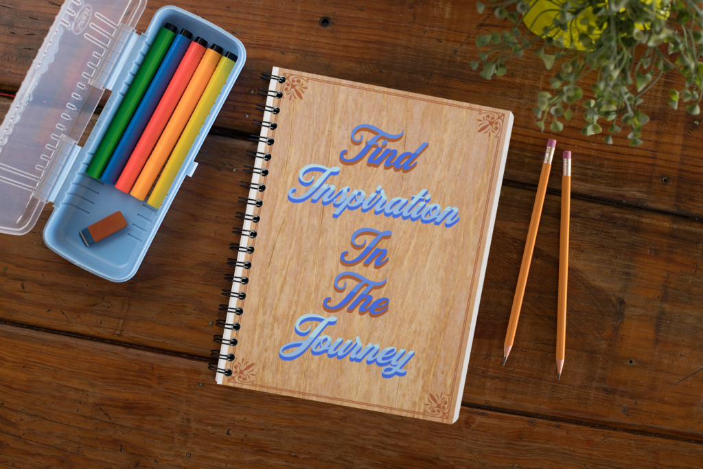 Spiral notebook with the message, Find Inspiration in the Journey. Notebook is on wooden desktop along with pencils.